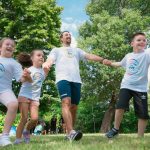 Group of joyful children playing outdoors with an instructor in a sunny park.